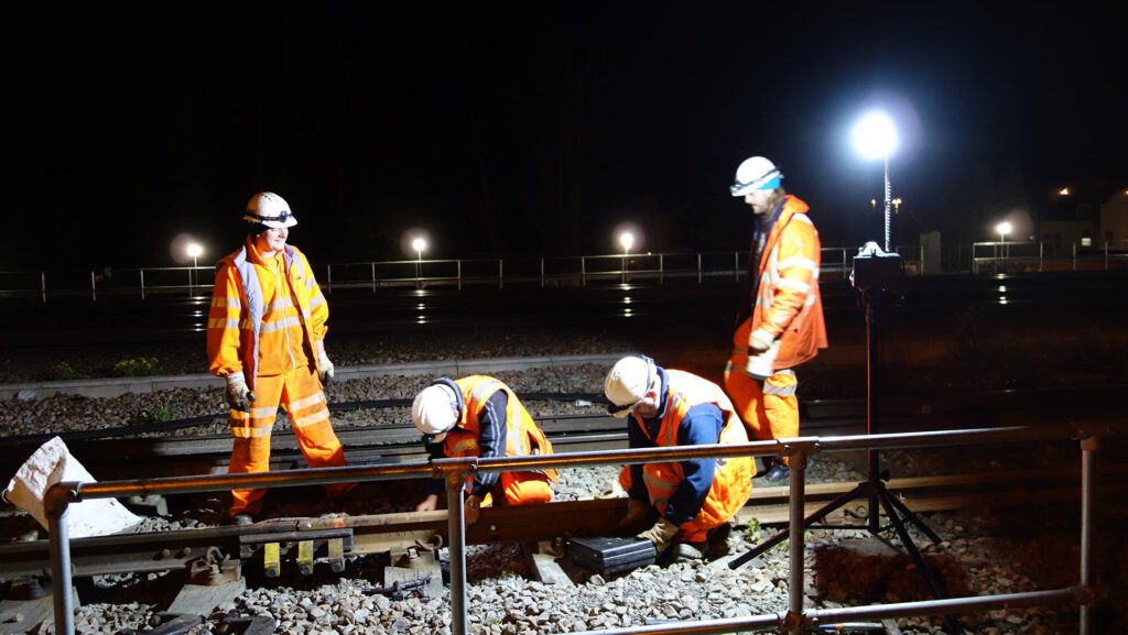 Workers conducting night-time rail inspection under battery-powered site lighting, demonstrating emission-free illumination for outdoor infrastructure work