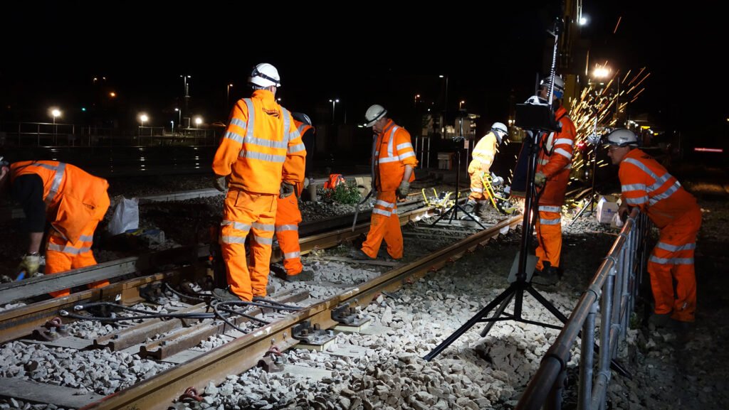 Railway maintenance crew working at night on track infrastructure, illuminated by portable rechargeable LED floodlights